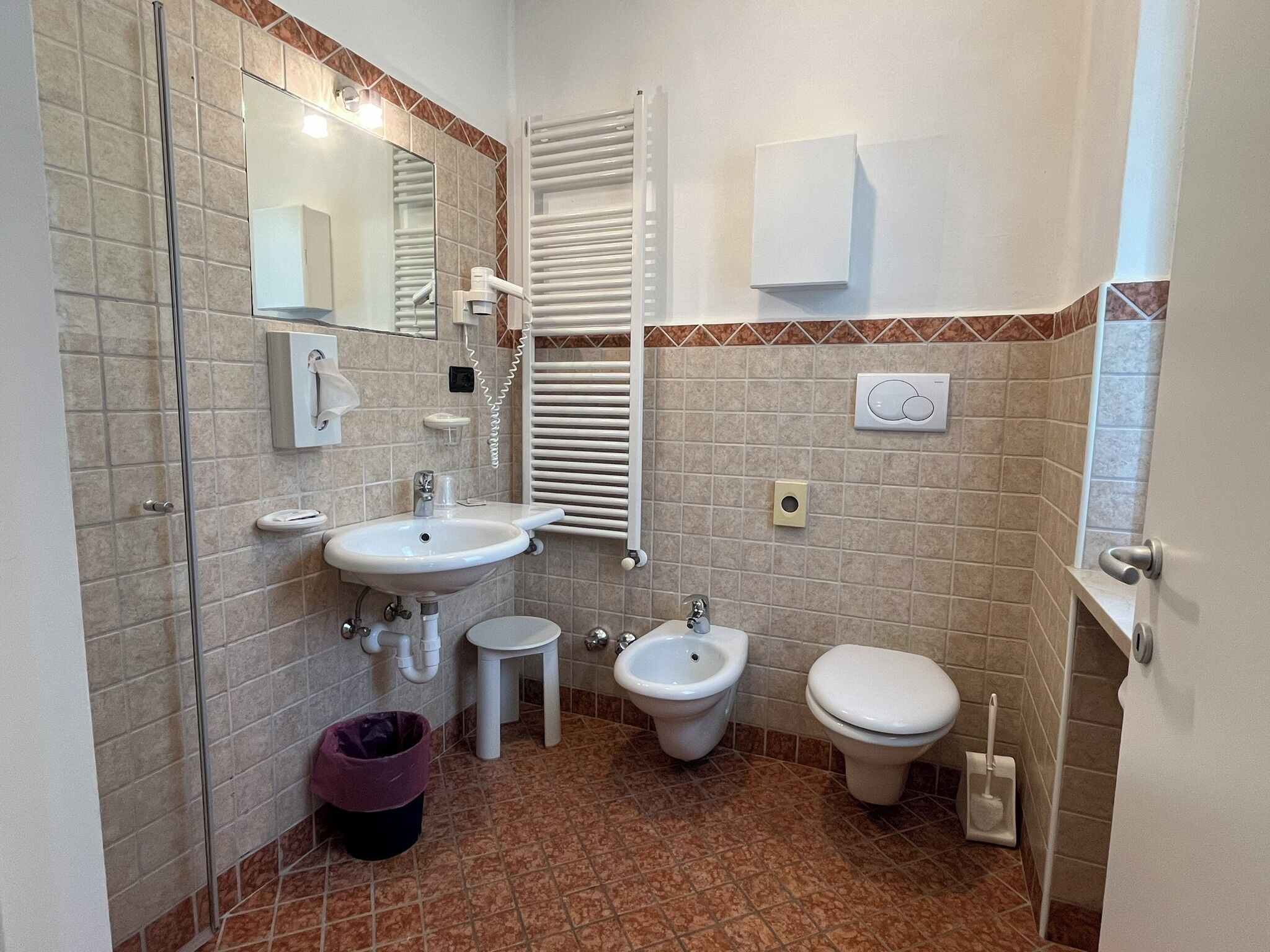 A compact bathroom with a sink, bidet, toilet, and a small mirror.