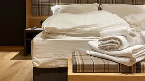 A neatly made bed with white linens and a plaid throw blanket, a bedside table with a lamp, and a wooden headboard. - Hotel Sayonara (Folgaria)