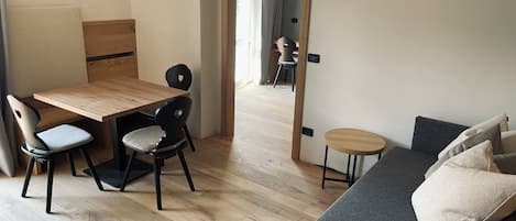 A room with a wooden dining table, two chairs, a grey sofa, and a small round table.