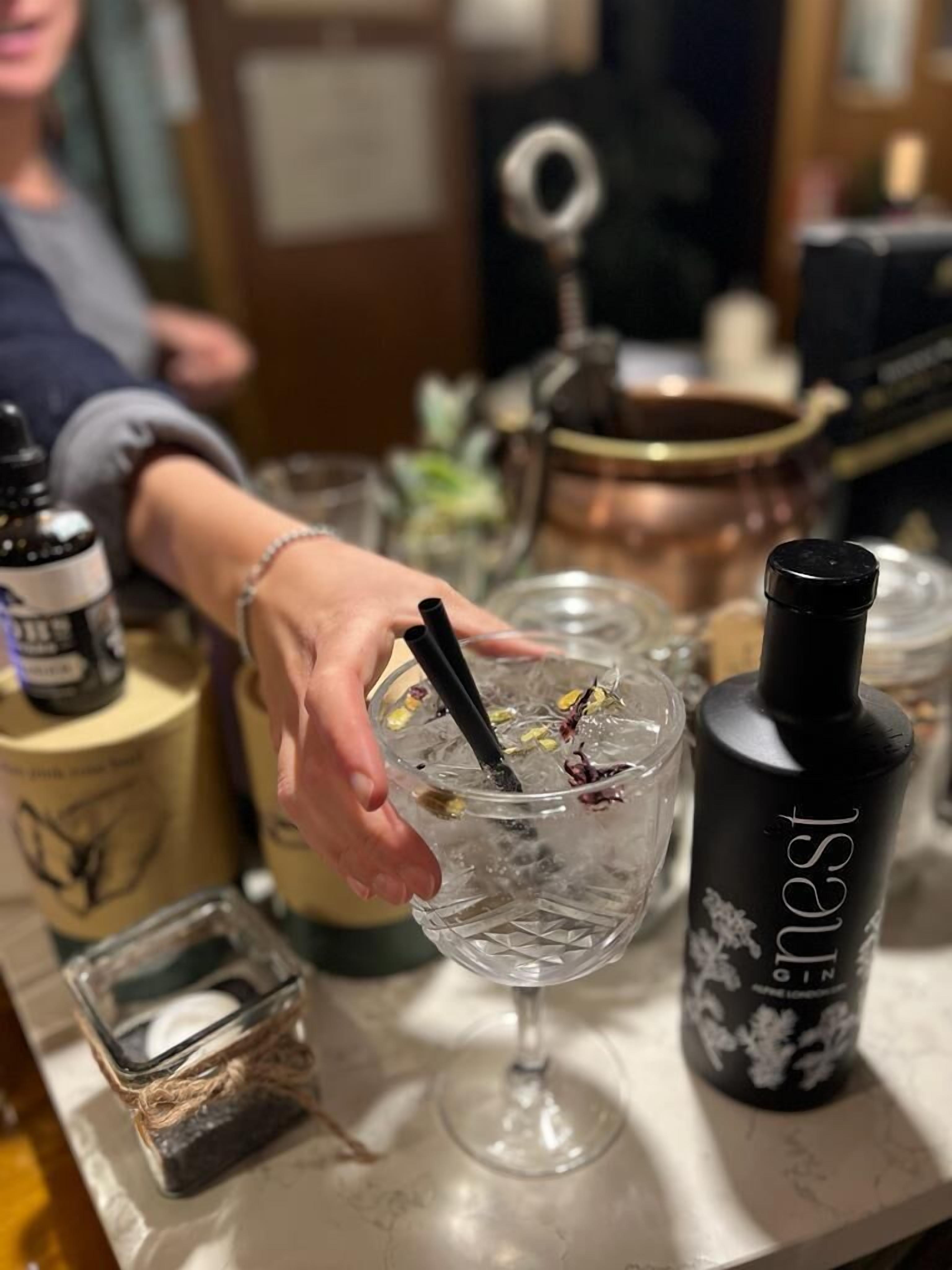 Zona bar con un bicchiere trasparente contenente una bevanda, una bottiglia di liquore 'nest' e una pentola di rame sullo sfondo.