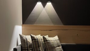 A modern room with a dark gray sofa, plaid cushions, a round wooden table, and a wall-mounted light fixture. - Hotel Sayonara (Folgaria)