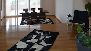 A spacious living room with a large window, a dining area with a table and chairs, and a potted plant. - Villa Konstantina (Nafplio)