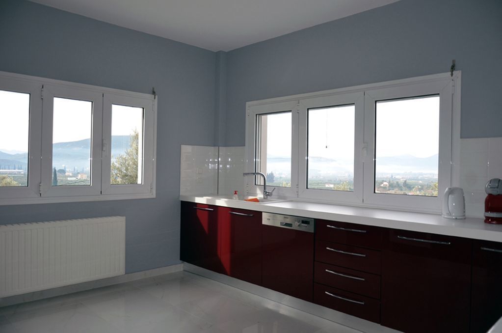 A modern kitchen with large windows, a white countertop, and dark cabinetry.