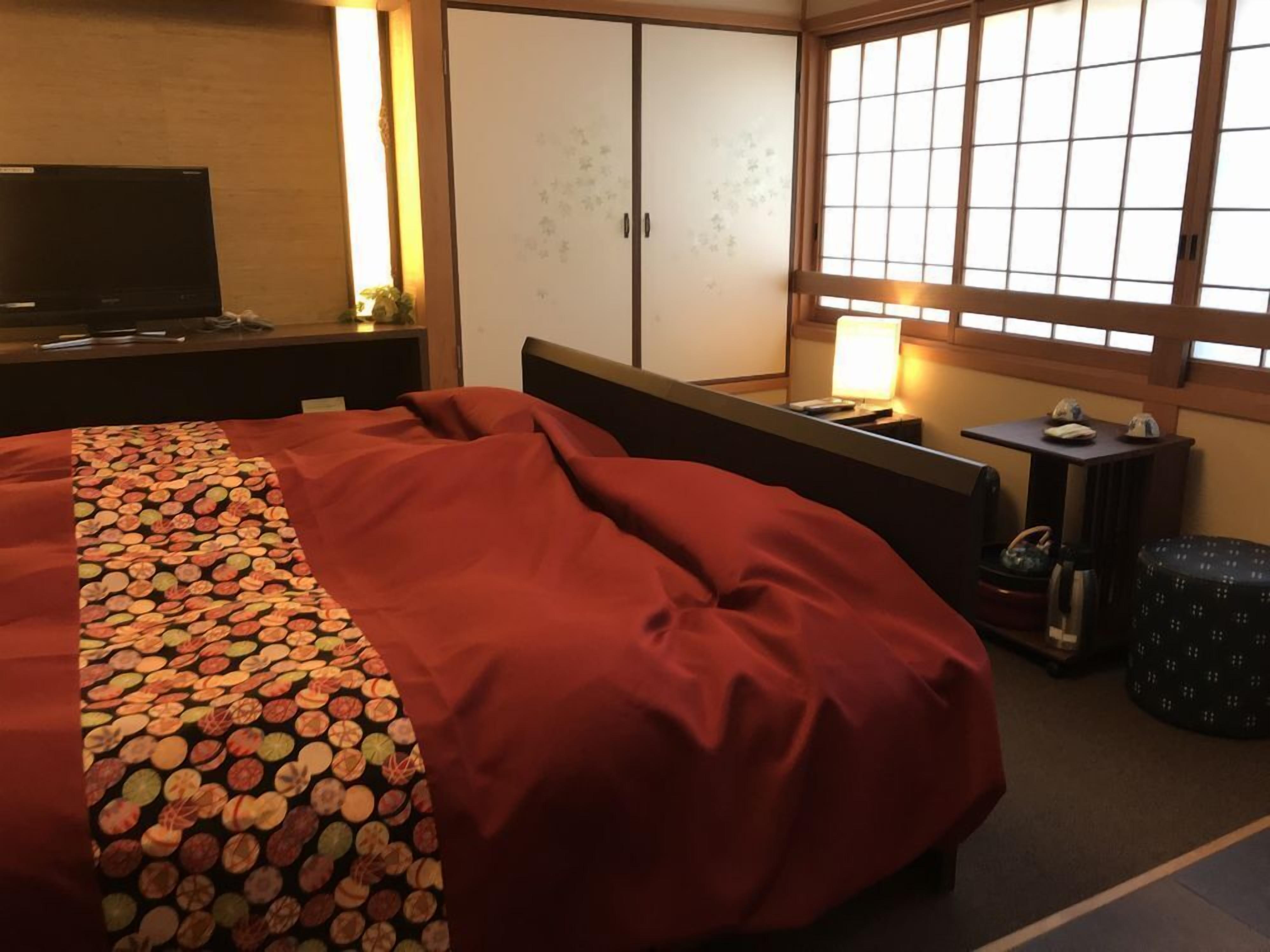 Habitación de hotel con cama, televisión, armario, ventana con vistas y mesita de noche con lámpara.