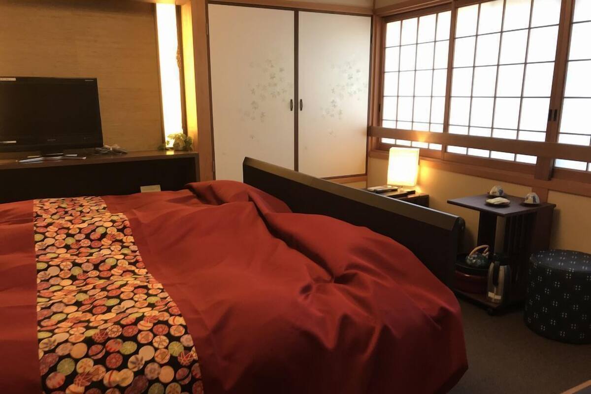 Ein Hotelzimmer mit Bett, Fernseher, Kleiderschrank, Fenster mit Blick und Nachttisch mit Lampe.