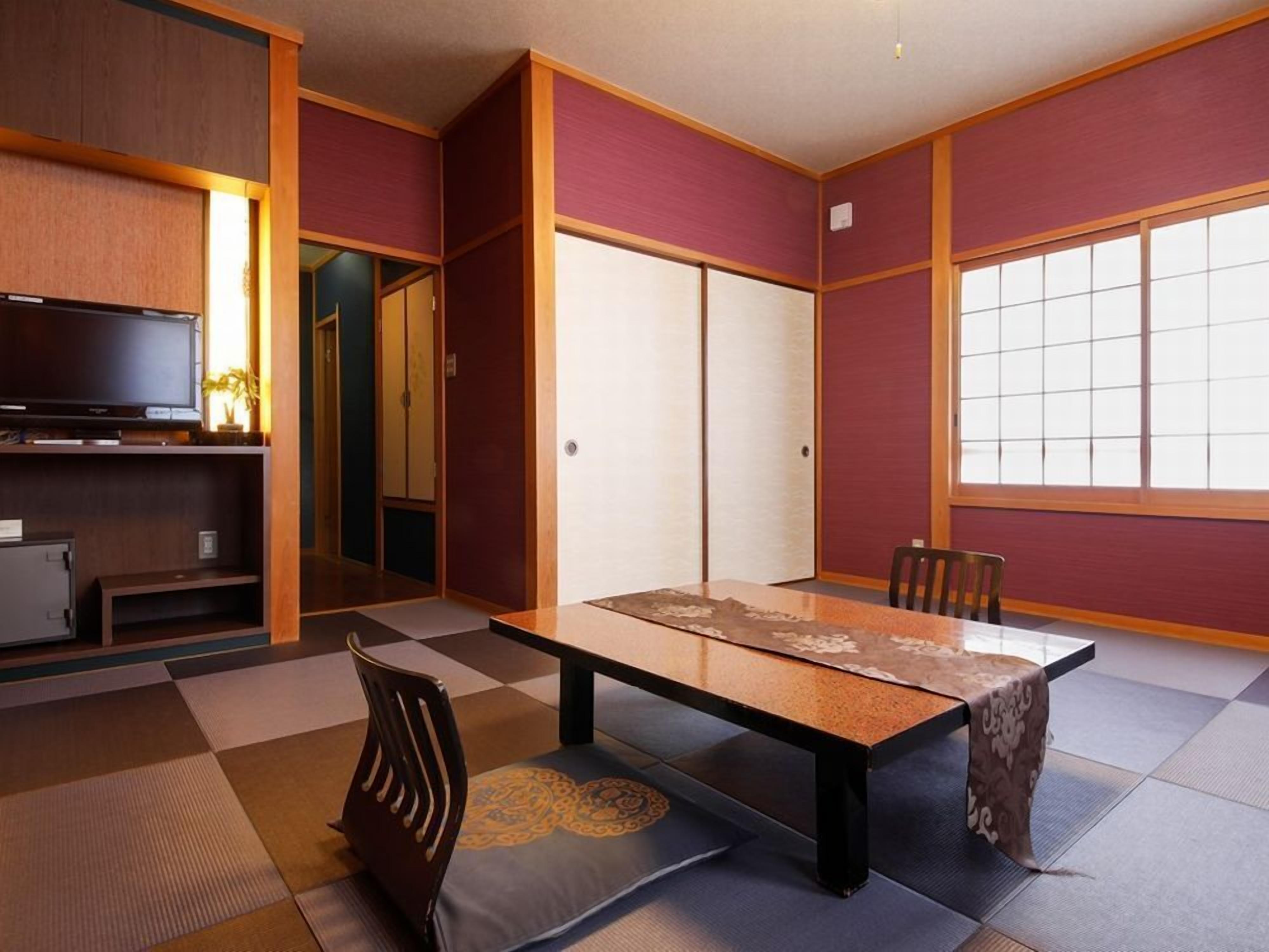 Une pièce de style japonais traditionnel, avec un sol recouvert de tatamis, une table basse, des chaises, un téléviseur et des portes coulissantes.