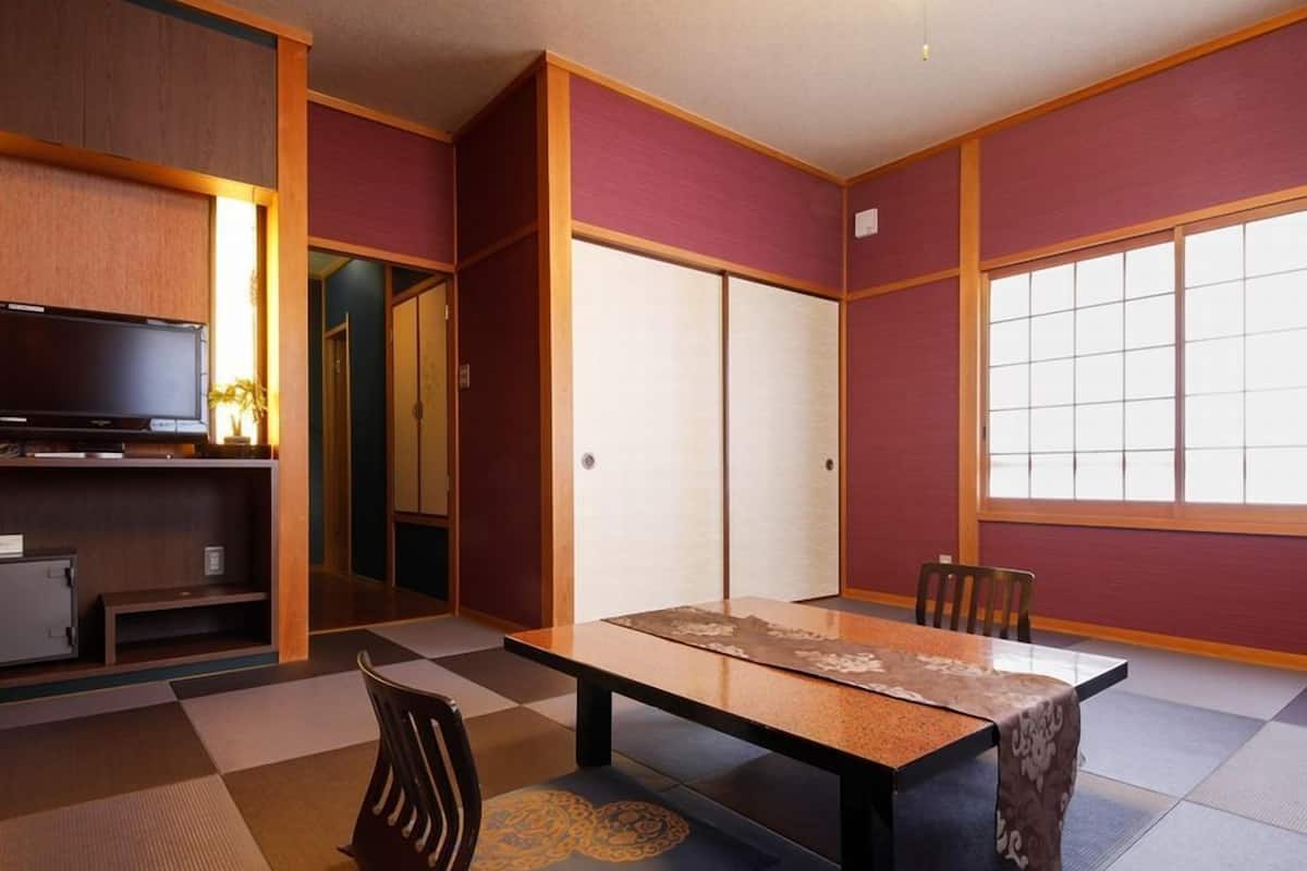 Ein traditioneller japanischer Raum mit Tatami-Bodenbelag, einem niedrigen Tisch, Stühlen, einem Fernseher und Schiebetüren.