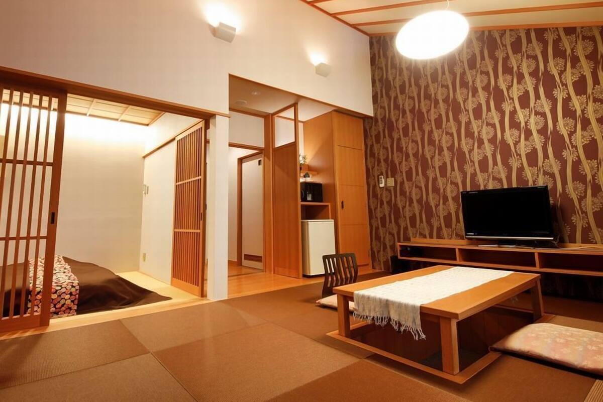 Ein traditioneller japanischer Raum mit Tatami-Boden, einem niedrigen Tisch mit weißem Tuch, einem Fernseher und Schiebetüren.