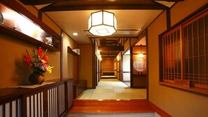 A traditional Japanese hallway with wooden flooring, a wooden railing, a hanging light fixture, and a vase of flowers on the left. - Kinosaki Onsen Ryokan Oyado Hakusan (Toyooka)