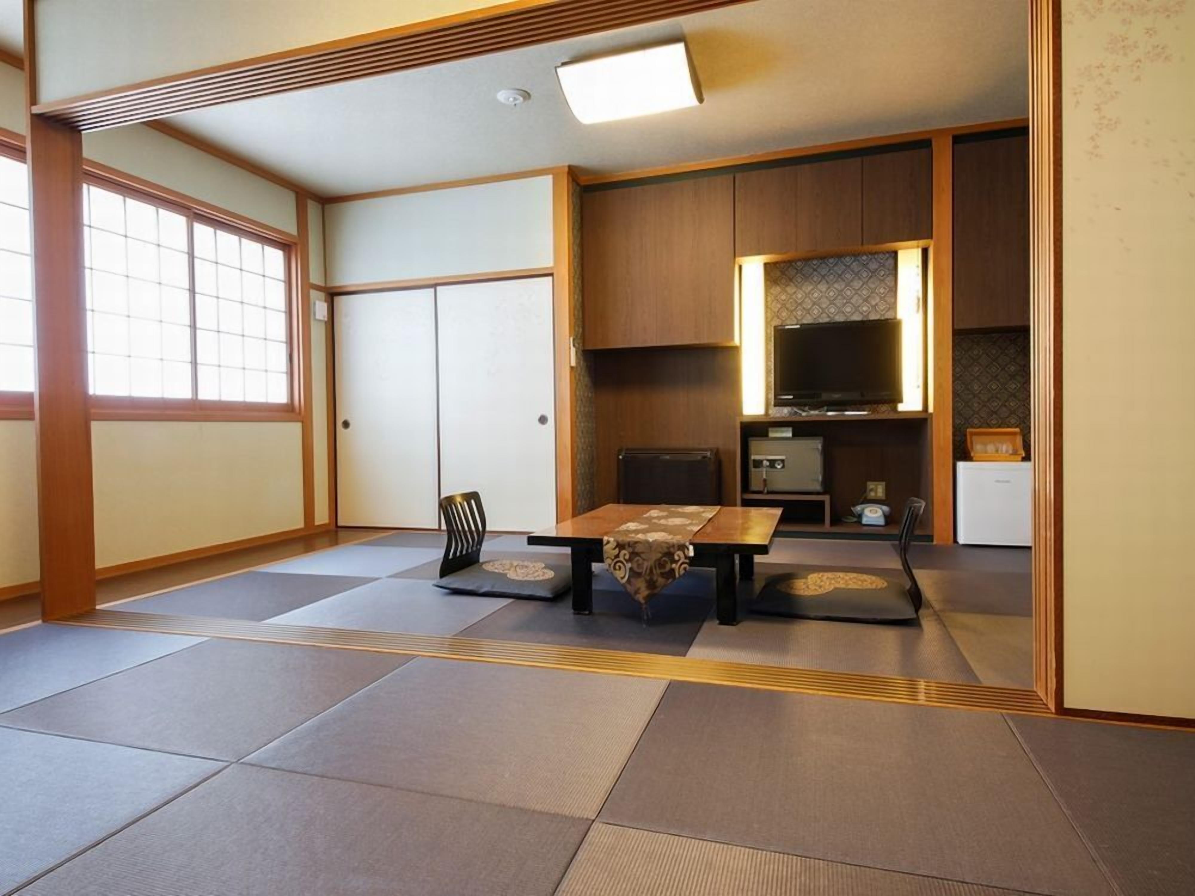 Une pièce de style japonais traditionnel, avec un sol recouvert de tatamis, une petite table basse avec des coussins, un téléviseur et un coin cuisine.