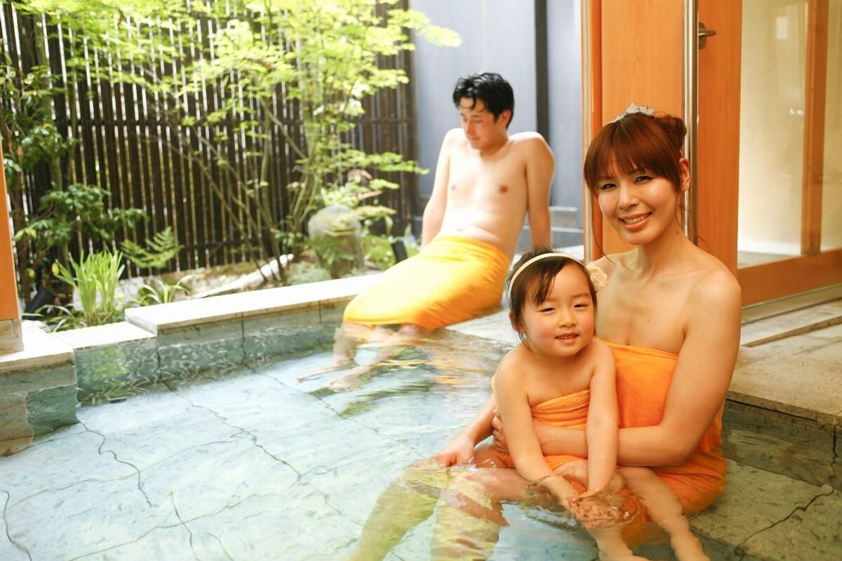 A family by a pool with a bamboo fence and a wooden door in the background.
