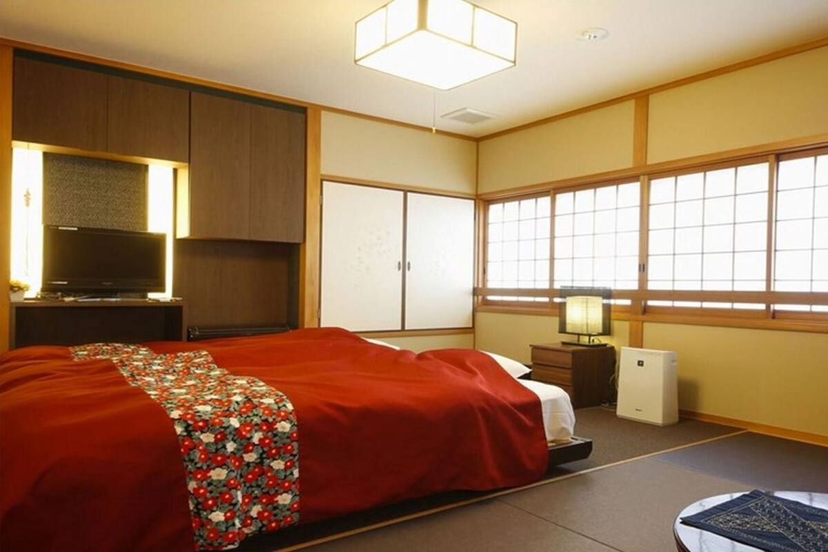 Ein traditionell gestaltetes japanisches Schlafzimmer mit Bett, Kleiderschrank, Fernseher und Futon.