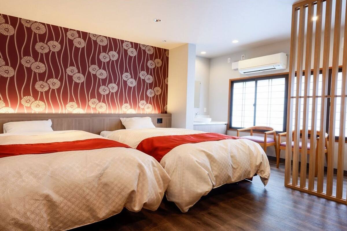 Ein Hotelzimmer mit zwei Betten, Holzboden, Wand mit Blumenmuster und Fenster mit Blick.