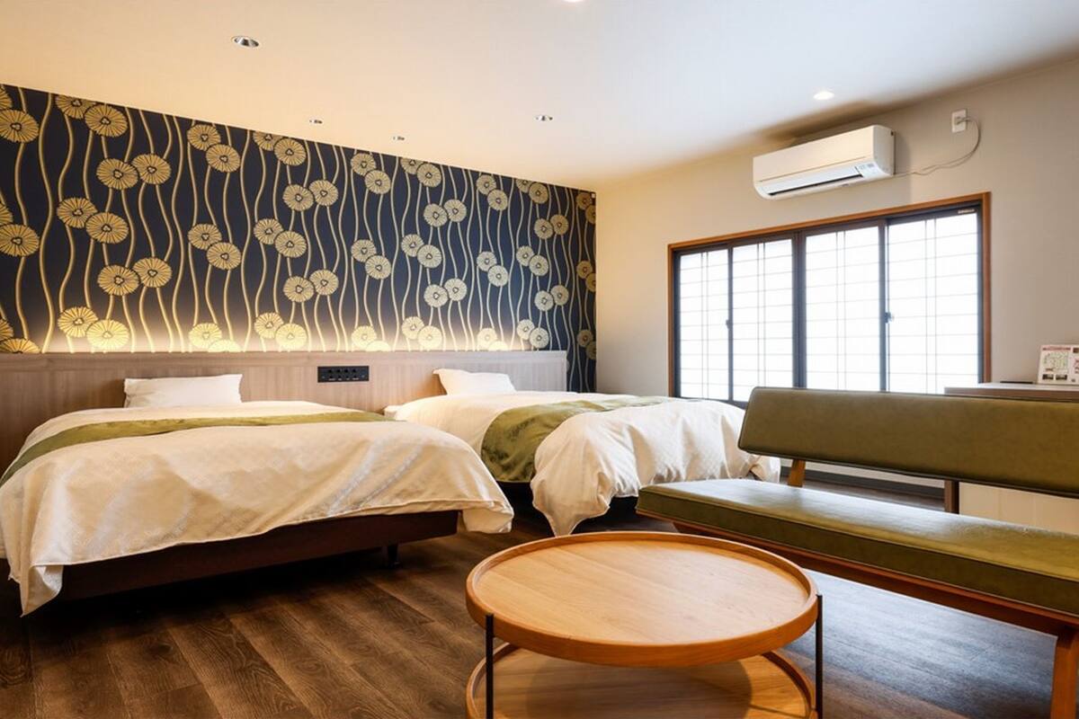 Ein Hotelzimmer mit zwei Betten, einer Bank, einem runden Holztisch und einem großen Fenster.