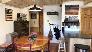 Une table à manger en bois avec des chaises, un luminaire suspendu, un buffet en bois et un comptoir de cuisine avec des tasses.
