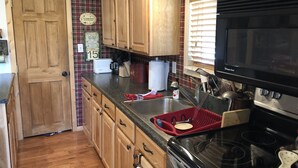 Une cuisine avec des meubles de rangement en bois, une cuisinière, un four à micro-ondes et une fenêtre avec des stores.