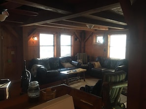 A cozy cabin-style room with a large wooden ceiling, two windows with blinds, a leather sofa, a wooden coffee table, and a ceiling fan. - Remote getaway-the national forest-Direct access to the ATV trails- Wolf Pen Gap (Mena)