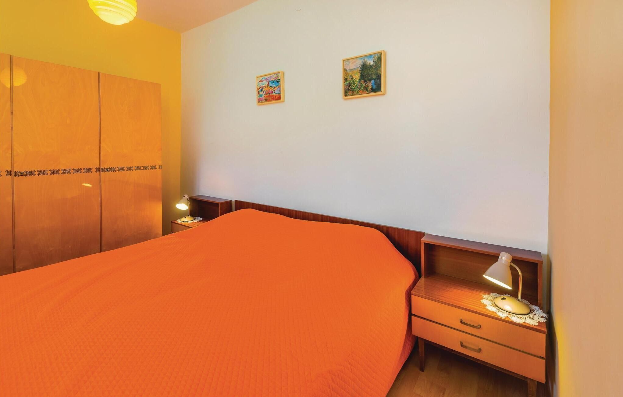 Een hotelkamer met een groot bed, een houten kledingkast, twee schilderijen aan de muur en een nachtkastje met een lamp.