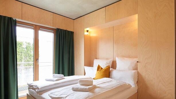A modern bedroom with a large bed, wooden paneling, and a view through a sliding door. - Kitz Boutique Hotel & Restaurant (Metzingen)