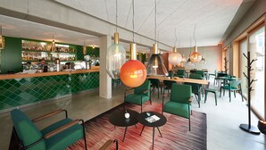 A modern bar area with green-tiled walls, a counter with various bottles, and green chairs and tables. - Kitz Boutique Hotel & Restaurant (Metzingen)