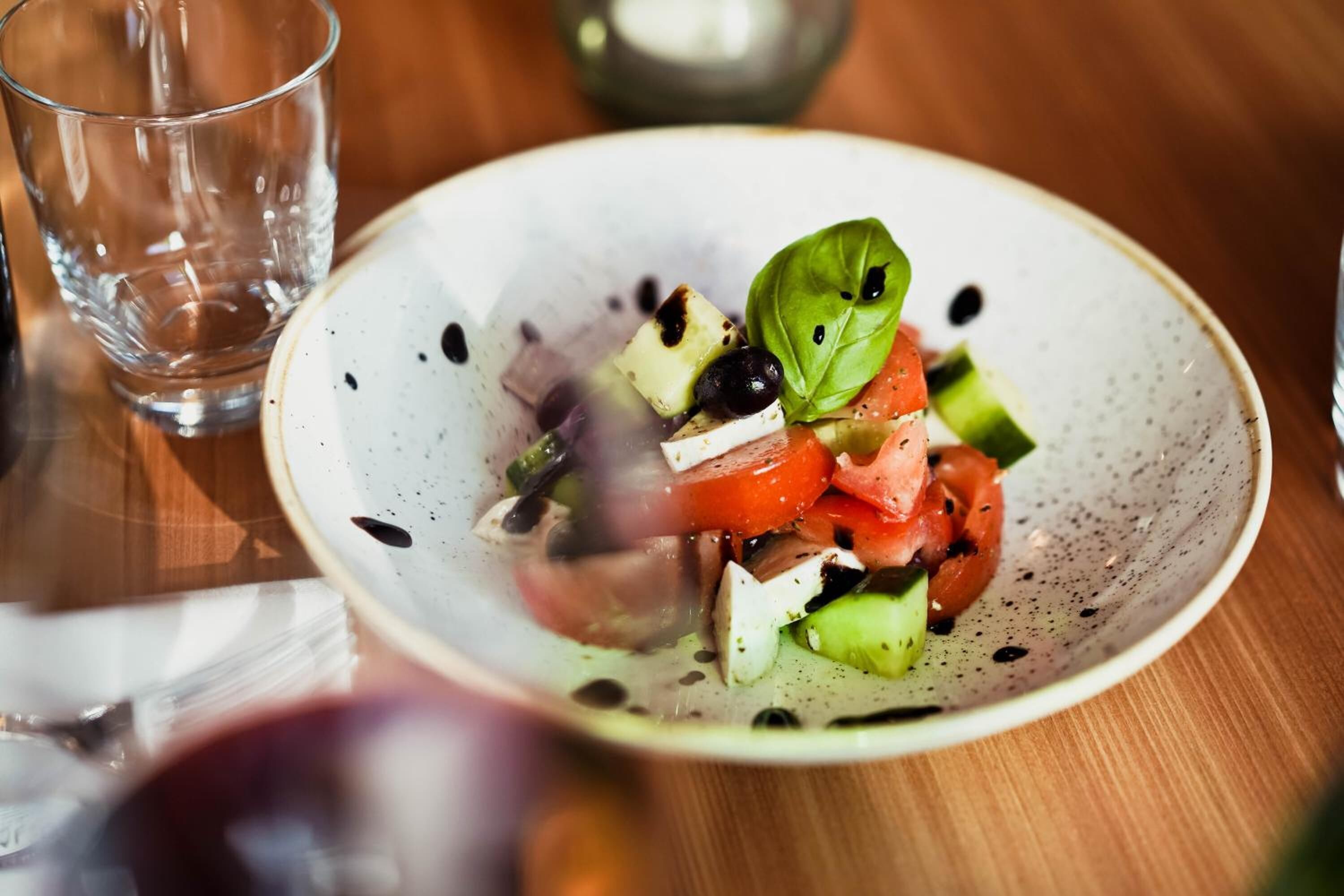 Una ensalada fresca con tomates, pepinos y aceitunas, servida en un plato de cerámica con manchas.