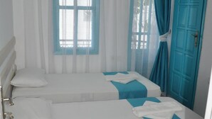 Une chambre d’hôtel avec deux lits, une fenêtre avec des bordures bleues, une porte bleue et un appareil de climatisation.