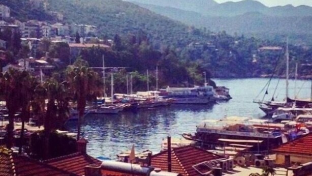 Un port de plaisance où sont amarrés des bateaux, entouré de collines et de bâtiments.