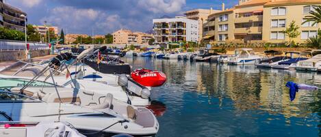 A marina with various boats docked, surrounded by buildings with balconies and a clear sky.
