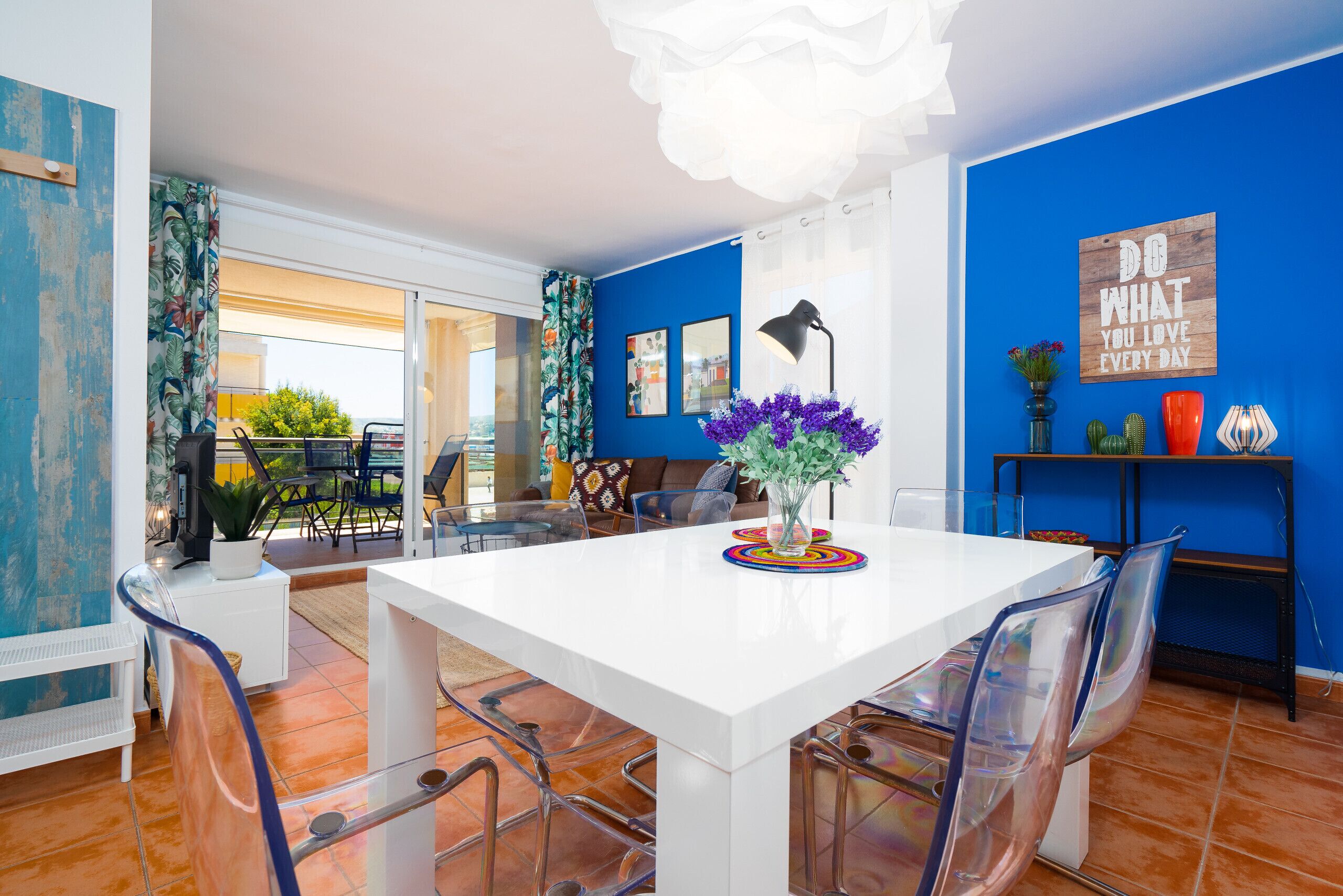A dining area with a white table, clear chairs, and a blue wall with a motivational quote.