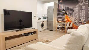 Un salon moderne doté d’un téléviseur à écran plat, d’un canapé, d’un coin repas avec une table et des chaises, d’un lave-linge et d’une cuisine équipée d’un four à micro-ondes.