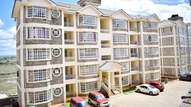 A multi-story residential building with balconies, a central staircase, and a parking area with cars. - Joy Comfort Homestay (Syokimau)