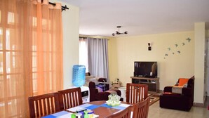 A dining area with a table set for four, a sofa, a television, and a water dispenser. - Joy Comfort Homestay (Syokimau)