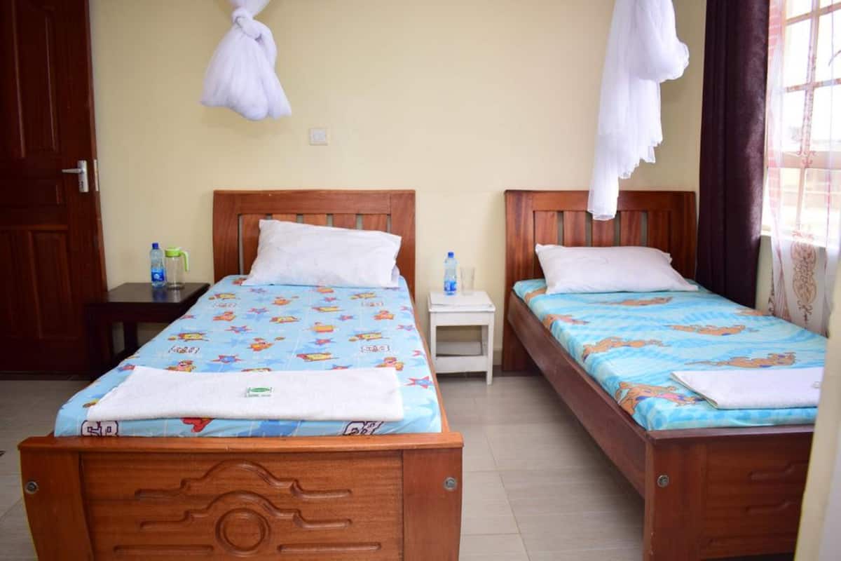 A hotel room with two wooden beds, each with a blue bedspread featuring cartoon characters. There are white towels on the beds, and a white robe hanging on the wall.