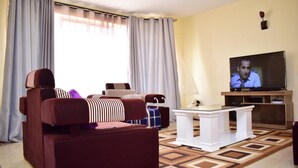A living room with a sofa, a coffee table, and a television. - Joy Comfort Homestay (Syokimau)