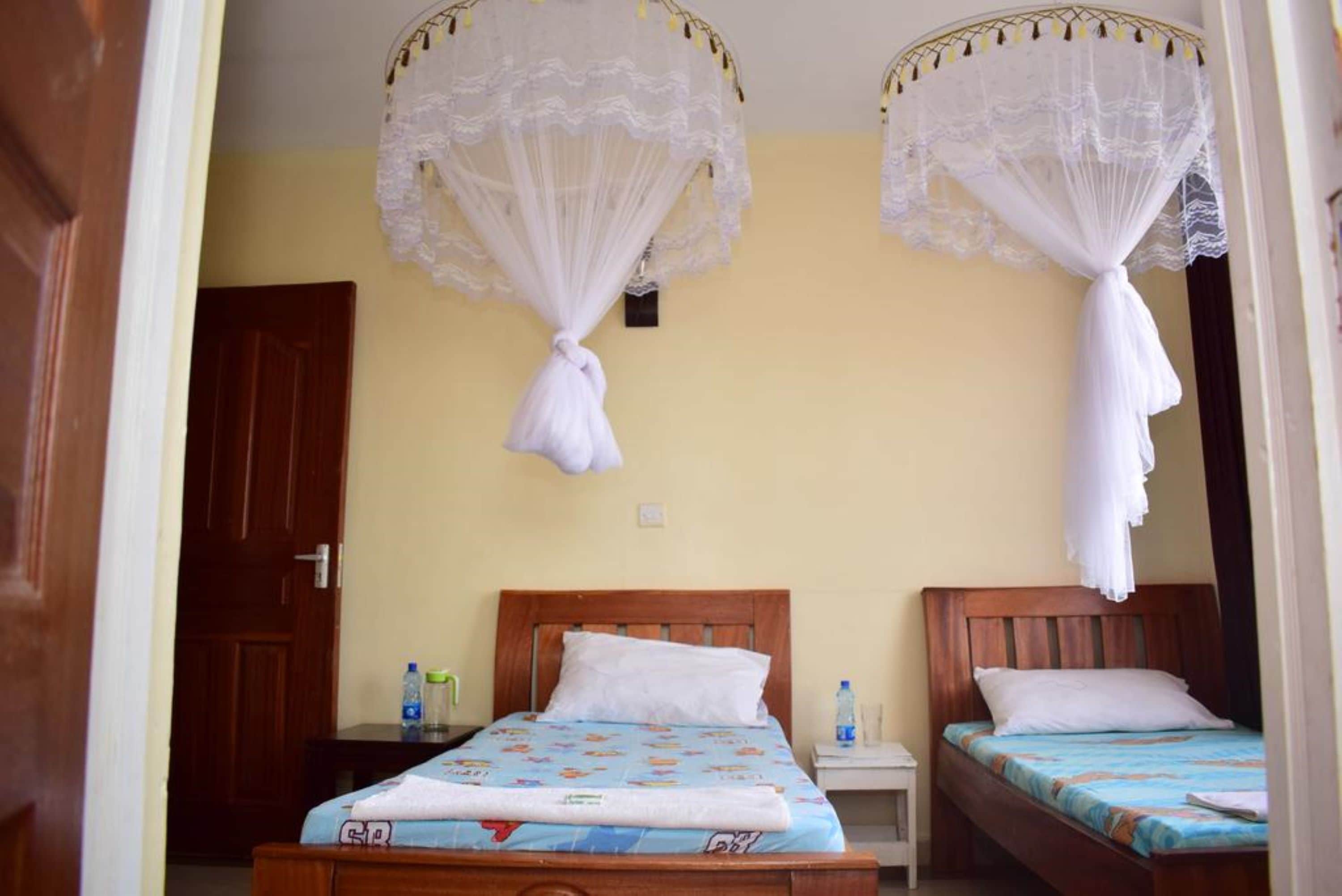 A room with two wooden beds, each with a blue bedspread and white pillows. There are two bedside tables with water bottles on them.
