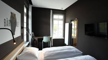 A hotel room with a bed, a desk, a chair, a TV, and a window.