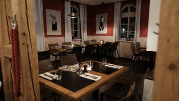 A restaurant with wooden tables and chairs, white curtains, and pendant lighting.