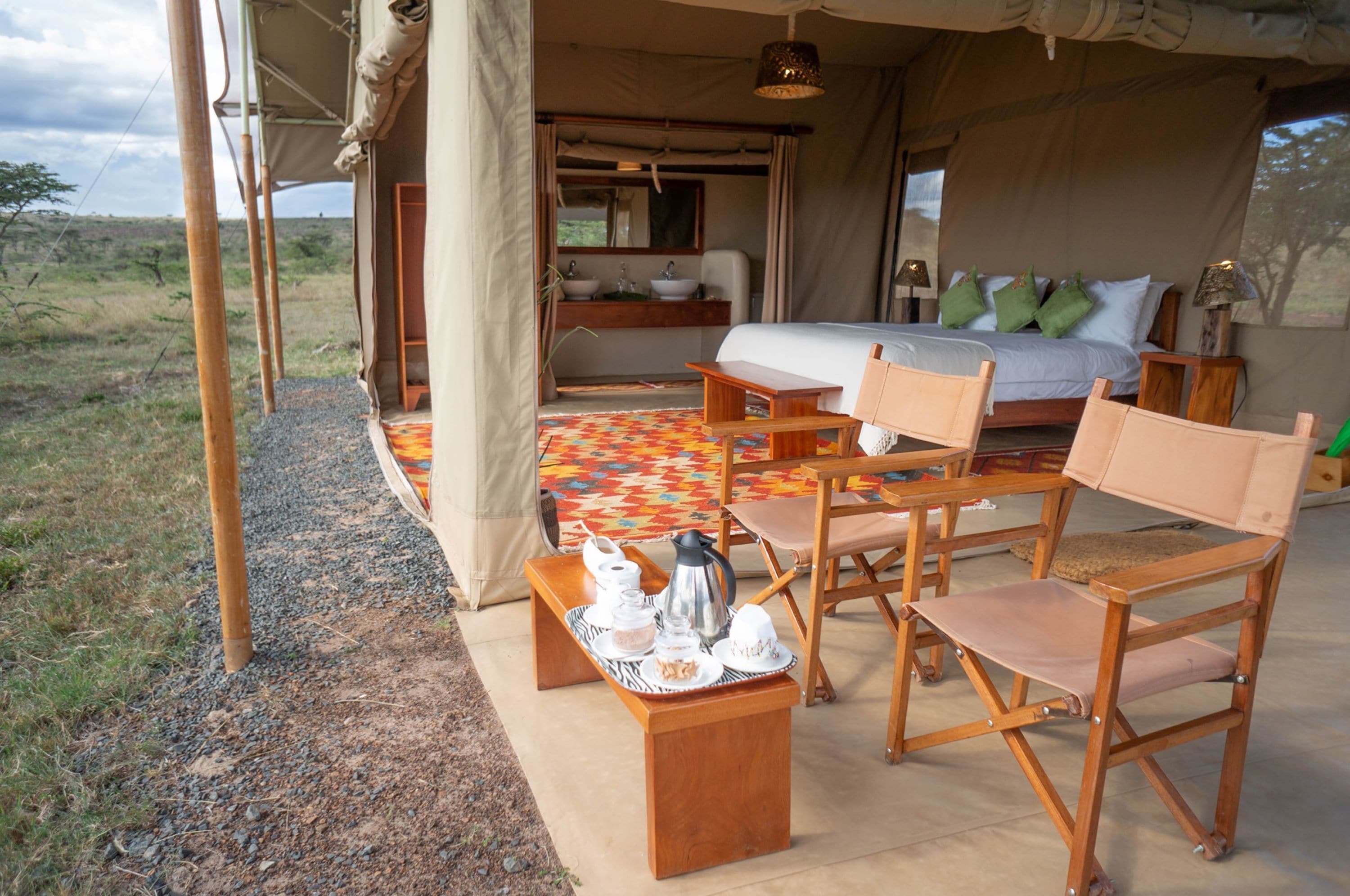 A tented accommodation with a bed, bedside table, and seating area.