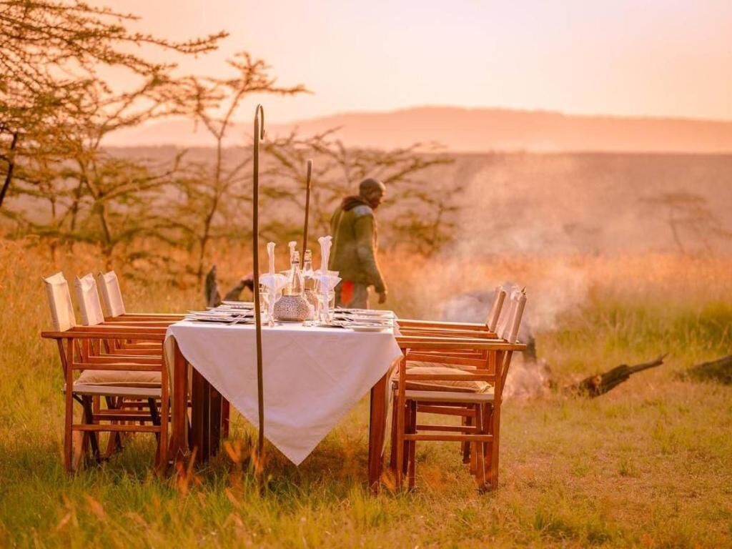 Mesa de comedor al aire libre con sillas, rodeada de paisaje natural y árboles.