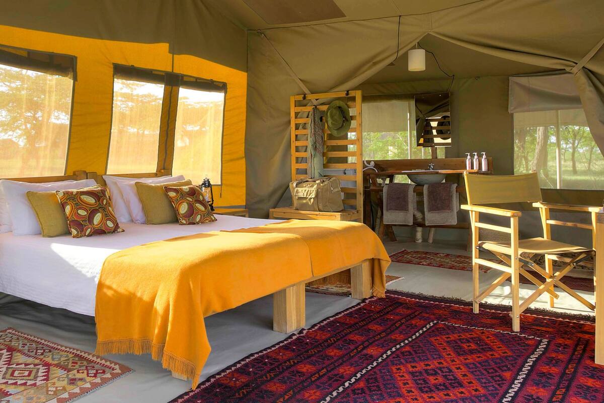 Una habitación tipo tienda de campaña con cama, muebles de madera y vistas al exterior.