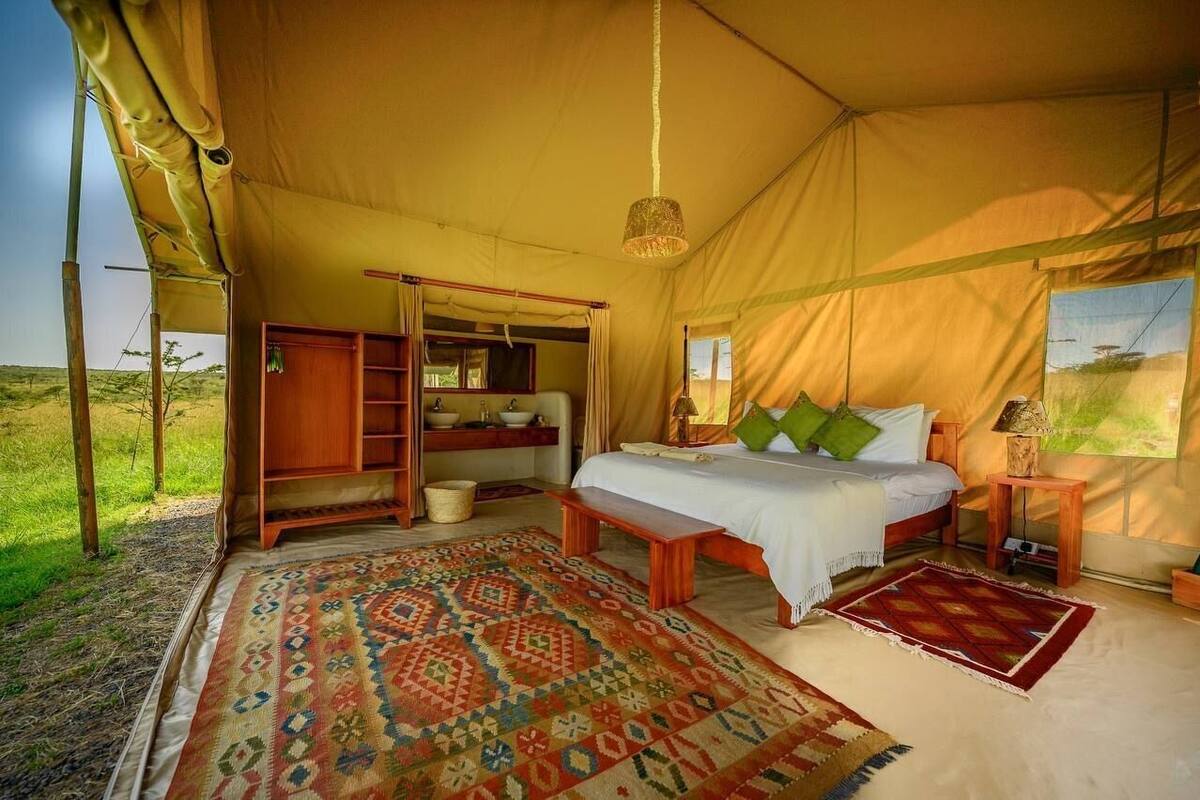 Una carpa con una cama, un banco de madera, un estante y una lámpara colgante.