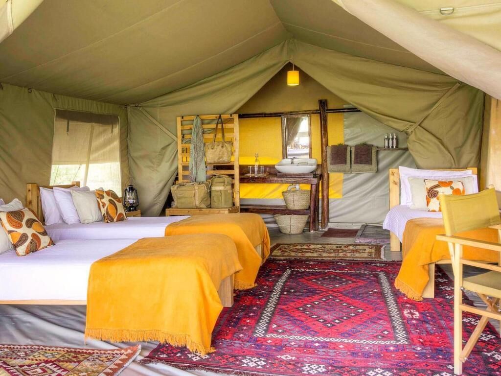 A tented accommodation with two beds, a small table, and a chair.