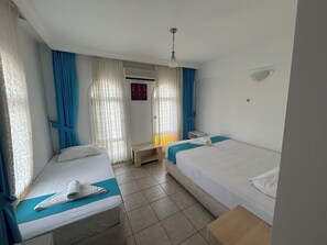 Ett hotellrum med två separata sängar, ett litet bord, en takfläkt och ett fönster med gardiner.