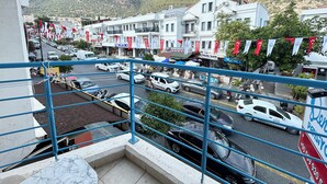Un balcón con vista a una calle bordeada de comercios y automóviles estacionados, con una extensa vista de montañas.