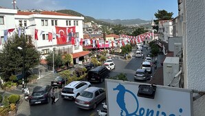 Vista de la calle con un letrero de un establecimiento llamado "Denizci Pansiyon" y un estacionamiento con coches.