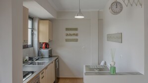 Ett kompakt kök med mikrovågsugn, vattenkokare och diskho. Det finns dekorativa väggdekorationer och en klocka.