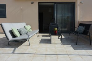 An outdoor seating area with a sofa, two chairs, and a small table with a potted plant.