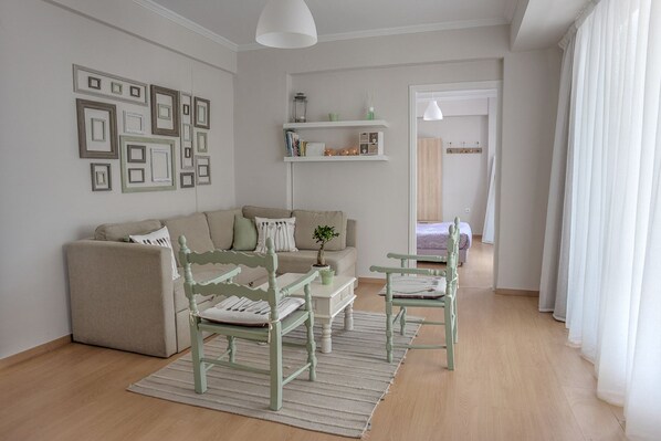 A living room with a sofa, two chairs, a coffee table, a bookshelf, and a door leading to another room.