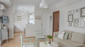 Ett vardagsrum med en soffa, två fåtöljer, ett soffbord och en tv. Det finns en dörr som leder till ett annat rum och en vägg med inramade tavlor.