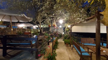 An outdoor patio area with stone flooring, wooden benches, and potted plants.